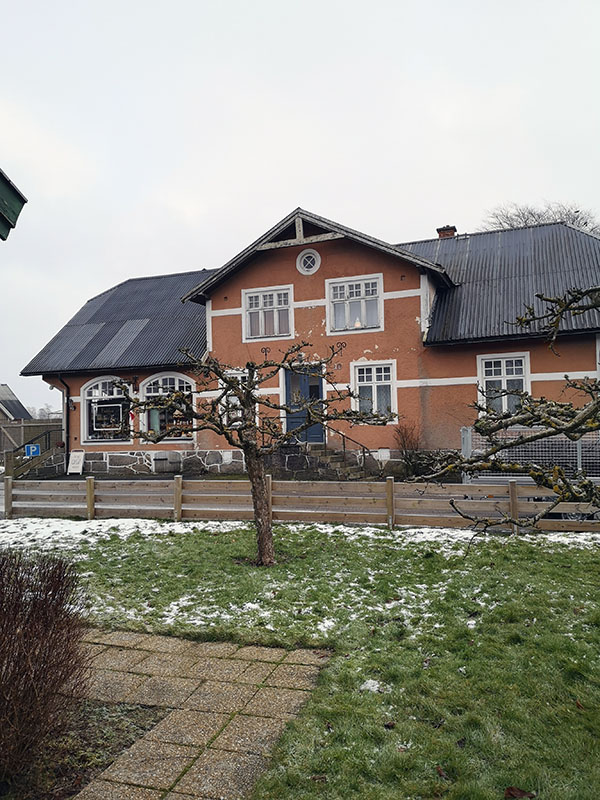 Trädgård med äldre träd som inte är beskurna. I bakgrunden en villaväg med ett hus.