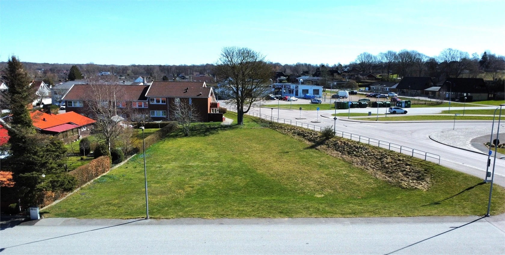 Bild av tom villatomt med gräs. Den omgärdas av vägar och hus.